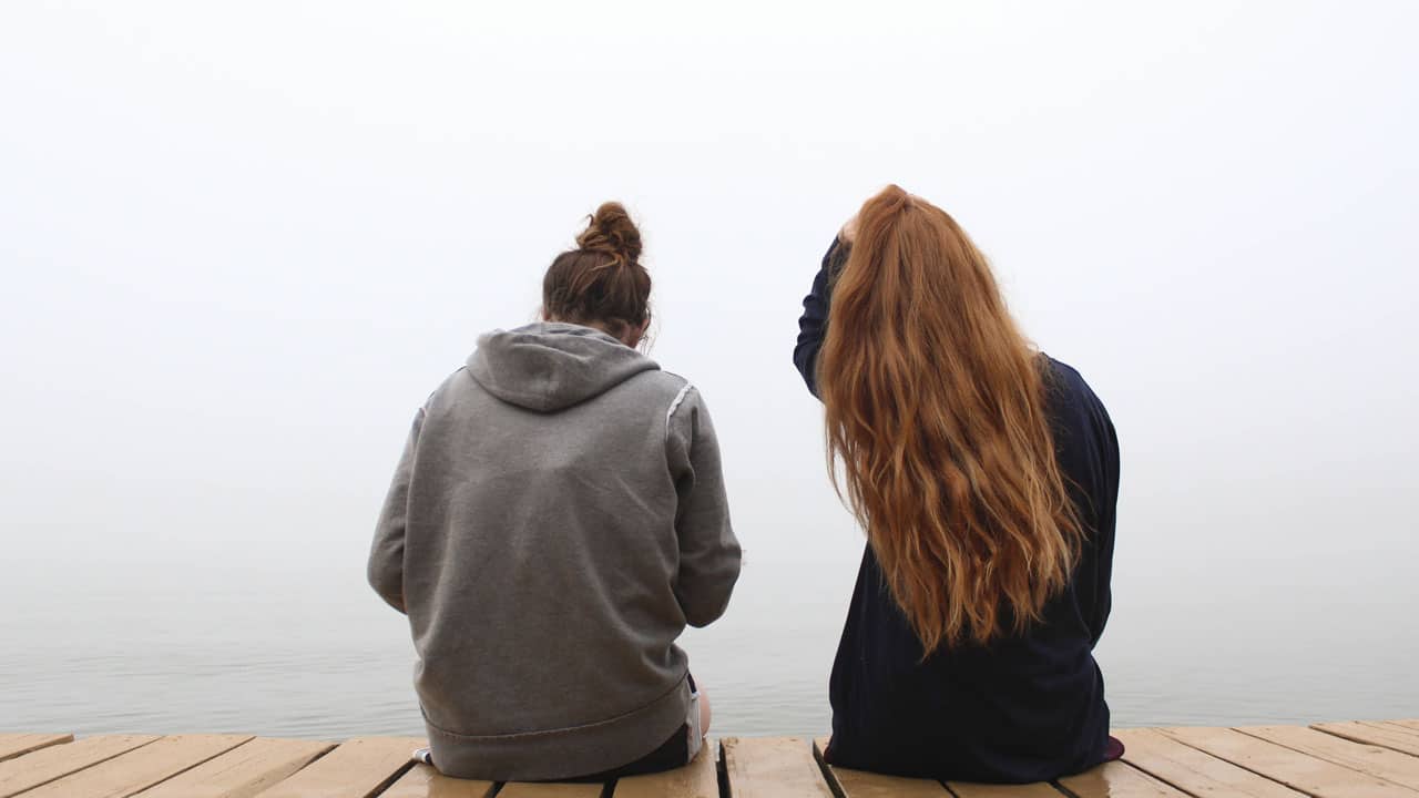 deux femmes de dos assises sur un ponton devant un lac illustrant la solidarité