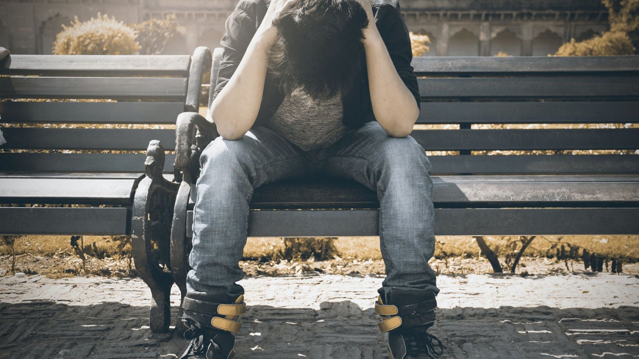 adolescent assis sur un banc la tête dans ses mains illustrant la tristesse du handicap