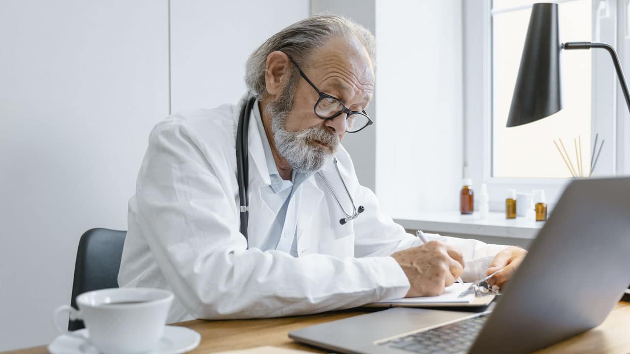 vieux médecin barbu penché sur son bureau el lisant un dossier illustrant une consultation