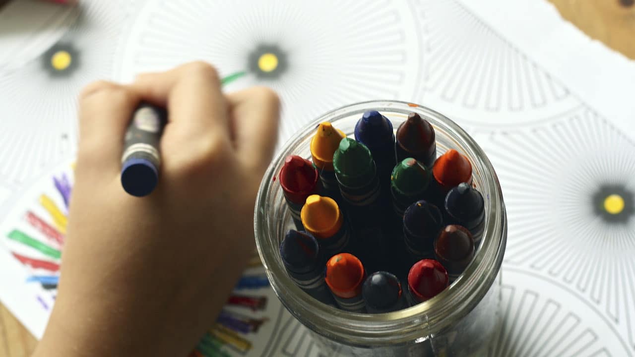 gros plan sur la main d'un enfant un pastel à la main avec à côté un gros pot en verre rempli de pastels