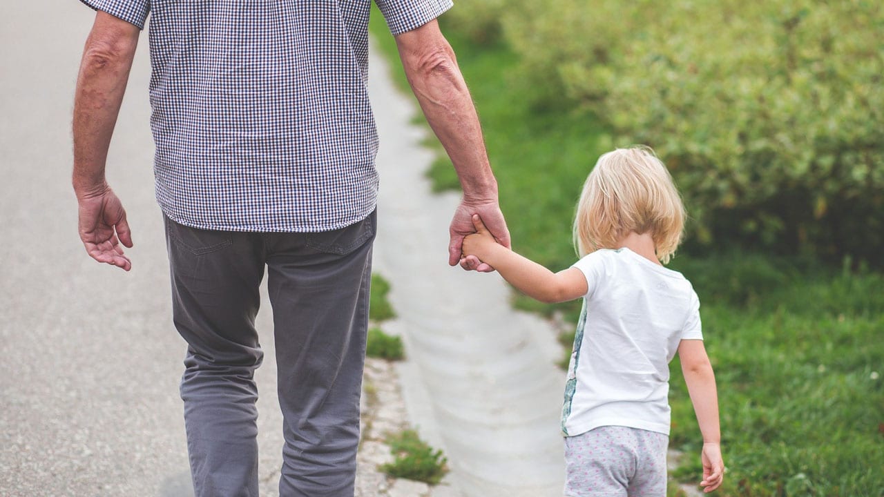 un père tenant son enfant par la main vus de dos